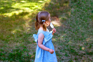 little girl in a blue dress eats ice cream in the park