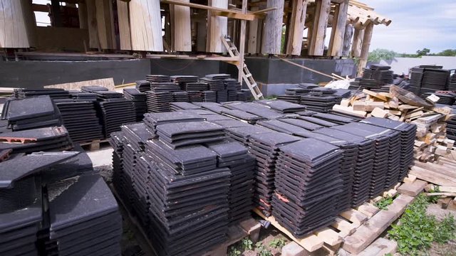 Construction site in progress to new house in countryside ecological area. Clip. Close up of roofing material, many black tiles lying on the ground.