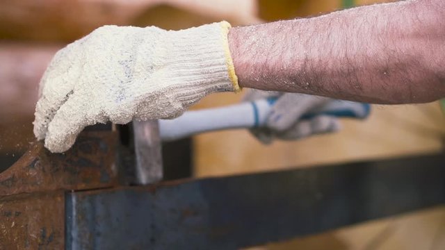 Worker wearing protective gloves hammering metal construction on wooden logs background. Clip. Carpentry works at construction site.