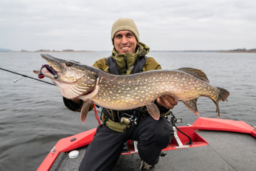 Happy fisherman with big pike fish. Boat fishing