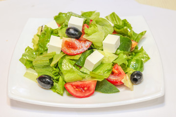 Photo of a Greek salad on a white plate with tomatoes, olives, feta cheese and herbs.