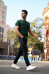 Full length of handsome young man wearing a green t-shirt and black jeans walking on a road near old heritage building , Men's fashion outdoor