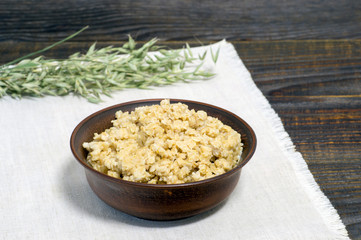 Oatmeal porridge in a ceramic brown bowl on a light linen napkin on a dark wooden table background.