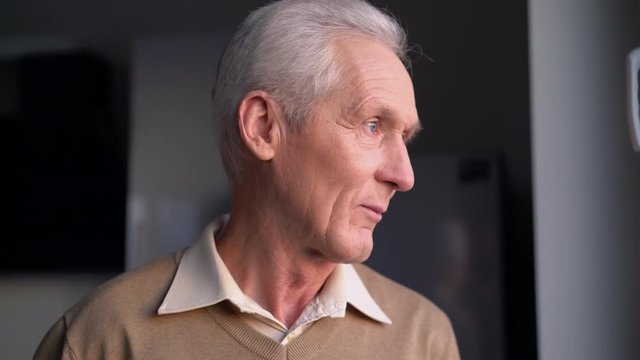 Sad thoughtful elderly man standing in room alone, concerned about retirement