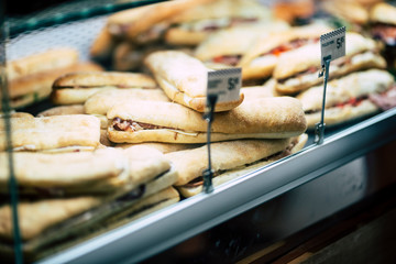 Mixed sandwiches in a bakery glass inside a shop - concept of fast tasty food with bread and salami - traditional lunch for workers concept