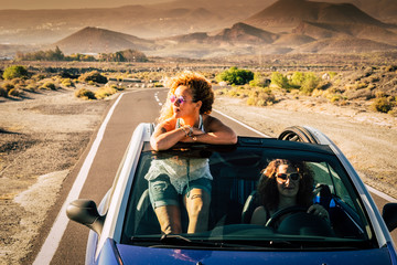 Couple of friends adult women traveling together free and independent on a convertivle car with mountsins and wild nature desert in background - travel and adventure people concept