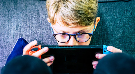 Young and concentrated caucasian child gamer with portable device playing with technology games...