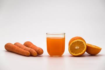Layout of oranges, carrots and fresh carrot and orange juice in a glass on a white background - detox fruit and vegetable organic juice
