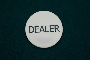 Dealer chip on green poker cloth in casino. Gambling concept