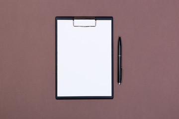 Clipboard with a white sheet and pen on a gray-dark background. View from above. space for text