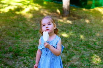 little girl in a blue dress eats ice cream in the park