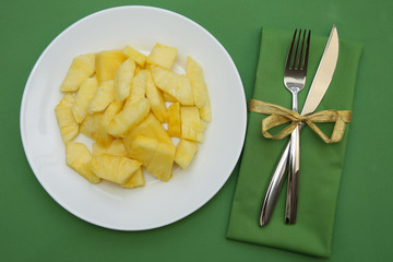 pineapple slices on a white plate on a green background with cutlery, fork and knife on a green cloth napkin. Flat lay. Top view. Restaurant menu. Vegetarian diet