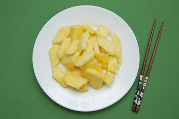 slices of juicy pineapple on a white plate on a green background with chinese chopsticks. Flat lay. Top view. Restaurant menu. Vegetarian diet