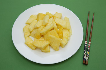 slices of juicy pineapple on a white plate on a green background with chinese chopsticks. Restaurant menu. Vegetarian diet