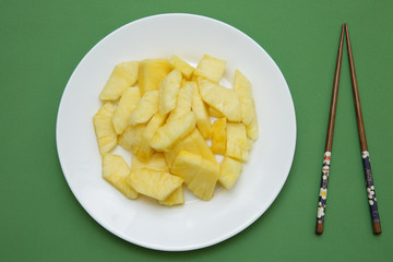 slices of juicy pineapple on a white plate on a green background with chinese chopsticks. Flat lay. Top view. Restaurant menu. Vegetarian diet