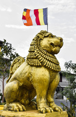 Brave Lion Posture sitting Statue in Gold with Buddhist flags in background