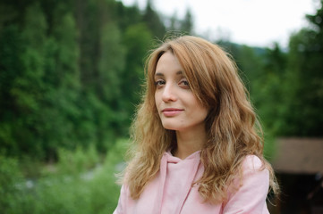 Naklejka premium Attractive young calm blonde woman in pink clothes with long hair on the hill with green forest background during spring or early autumn in the mountains.