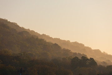 Warm sun glowing in misty morning light along tree line. 