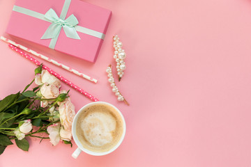 Flatlay pink coral background, the cup of cappuccino coffee and sweets macaroons, spring white roses, giftbox, beauty stuff - hair pin, nail polish and parfum. Best gift for woman