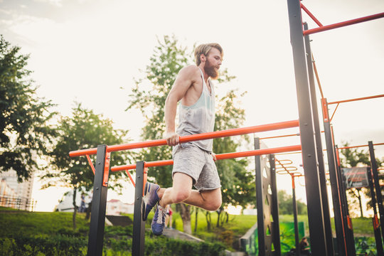 Fit Man Workout Out Arms On Dips Horizontal Bars Training Triceps And Biceps Doing Push Ups. Handsome Man Doing Exercise On Parallel Bars. Male Athlete Exercises On Parallel Bars Outdoor