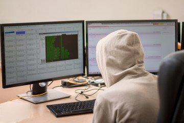  A hacker breaks into the protection of the enterprise. Cyber security concept. A young guy in a hood looks at the monitors. A teenager sits in an office chair and works at a computer.