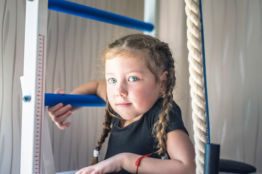 Portrait of young and beautiful gymnast in gymnastic leotard. Little girll goes in for sports on climbing frame. Sports child climbs the stairs. Children's sports concept