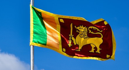 Waving colorful Sri Lankan Lion Flag in cloudy blue sky background 