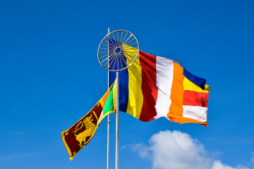 Waving colorful Buddhist Flag and Sri Lankan Lion Flag under the Dharma Chakra symbol in cloudy blue sky background 