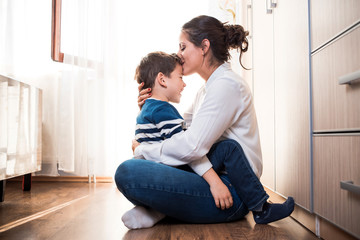 Beautiful young mom and her son. Mom is kissing her kid in the forehead.