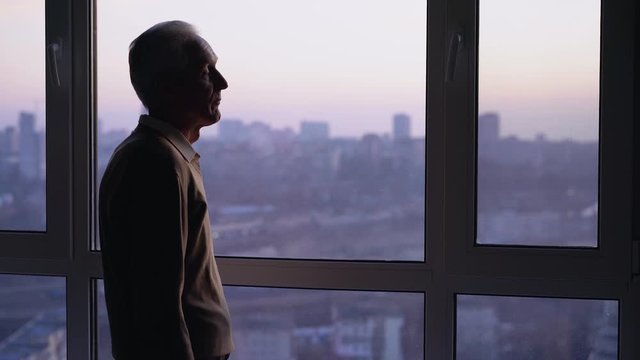 Exhausted sick man standing alone by window, health problems, loneliness crisis