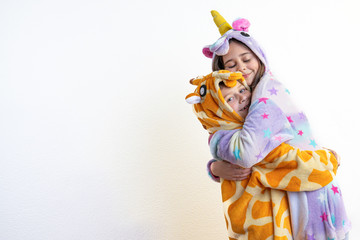 Cute children, boy and girl, brother in giraffe pajamas and sister in unicorn pajamas hug each other, isolated over white background, lovely family concept