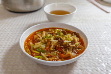 TURPAN, XINJIANG / CHINA - October 6, 2017: White plate with Laghman noodles. Ingredients include vegetables like celery, red and green pepper and lamb meat. In the back a cup of tea. Xinjiang food.
