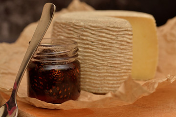 cheese head on a wooden board and kraft paper with a jar of pine cone jam on a dark background