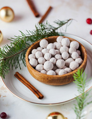 A handful of cranberries in powdered sugar on a wooden plate, next to cinnamon sticks, fresh cranberries, spruce branches and Christmas balls.