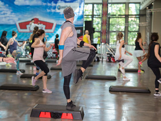 Fitness Workout in Gym: People doing Exercises in Class with Step Platform, Music and Teacher on Stage