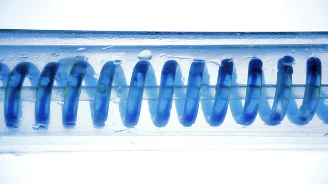Blue fluid flowing, spiraling horizontally from left to right. Scientific laboratory condenser. Scientific lab experiment. Colorful chemicals processing through glass tube. Cooling organic liquids.