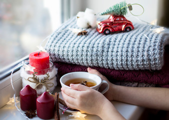 cup of warm tea in small children's hands with New Year paraphernalia and lights