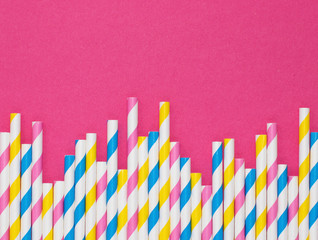 Border of paper straws with stripes against a hot pink background with copy space