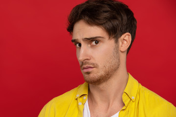 worried man in yellow shirt looking at camera isolated on red background. Face expressions concept