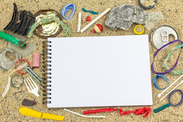 Top view of empty notebook on sand background surrounded by real plastic pollution found on beach, reduced plastic pollution, zero waste, green environment eco concept with copy space