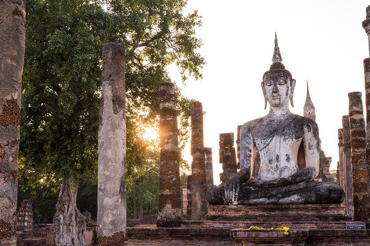 Sculpture standing buddha image of Wat Mahathat in the National Park of Sukhothai in Thailand at sunset. Travel to Asia and holidays concept. Buddhist religion, ancient art and asian heritage culture.
