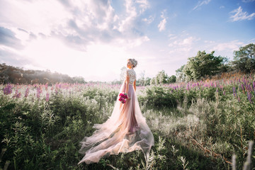 Beautiful girl in a field with flowers in pink sundress in the sunset