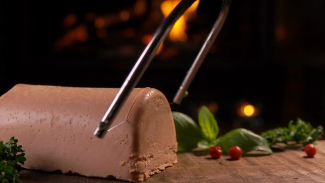 Special string knife cuts foie gras into slices on a wooden board on the background of a burning fireplace