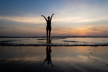 Silhouette of a girl standing in the water with her arms raised and her reflection in the water