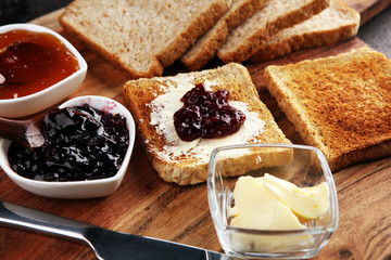 Toast bread with homemade strawberry jam and apricot marmalade on rustic table served with butter...