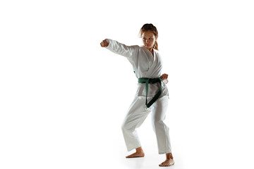 Confident junior in kimono practicing hand-to-hand combat, martial arts. Young female mongol fighter with green belt training on white studio background. Concept of healthy lifestyle, sport, action.