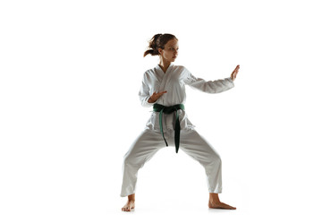 Obraz premium Confident junior in kimono practicing hand-to-hand combat, martial arts. Young female mongol fighter with green belt training on white studio background. Concept of healthy lifestyle, sport, action.