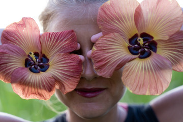 Woman with painted lips covering her eyes with two exotic flowers