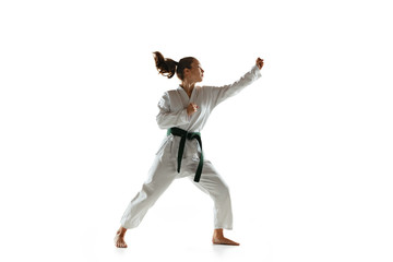 Confident junior in kimono practicing hand-to-hand combat, martial arts. Young female mongol fighter with green belt training on white studio background. Concept of healthy lifestyle, sport, action.