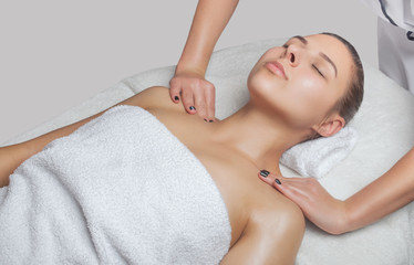 Fototapeta na wymiar Masseur makes a relaxing massage on the face, neck, shoulders and collarbones of a young beautiful woman in a spa. Cosmetology and massage concept.